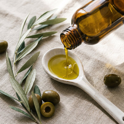 Organic extra virgin olive oil pouring from amber bottle with fresh olives